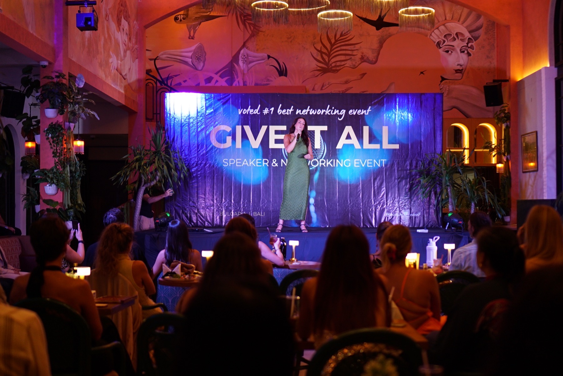 Amy Schwab speaking on stage to a full room at a Give It All networking event